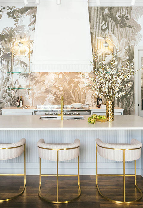 In the middle of Kitchen White Kitchen Countertop and Base Cabinets With White Chair Seat With Golden legs. White Kitchen Hood and Printed Kitchen Walls