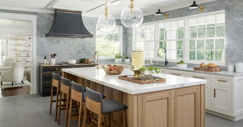 Marble countertop above wooden cabinets with wooden chairs, textured marble wall and dark grey French kitchen ranges with dark grey hood
