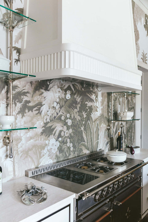 Black kitchen cabinets with silver burners and fancy stove with white custom kitchen hood and green printed wallpaper