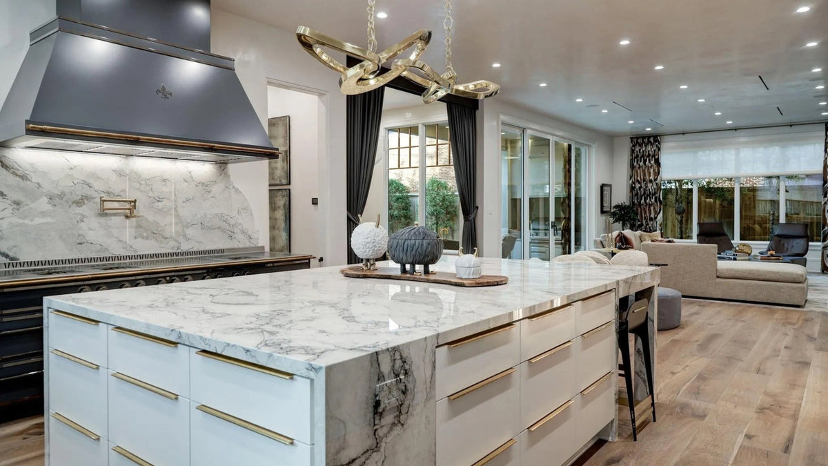 Large marble kitchen island with a waterfall edge and gold hardware in a modern open-concept kitchen