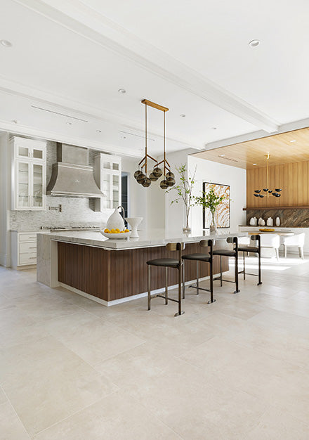 Luxury French-style kitchen featuring a navy blue La Cornue range and stainless steel range hood set within a rustic stone and white brick archway. The room has a white kitchen island with a butcher block countertop and open shelving, white floor-to-ceiling cabinetry with a built-in blue refrigerator, and is illuminated by a large arched black-grid window.