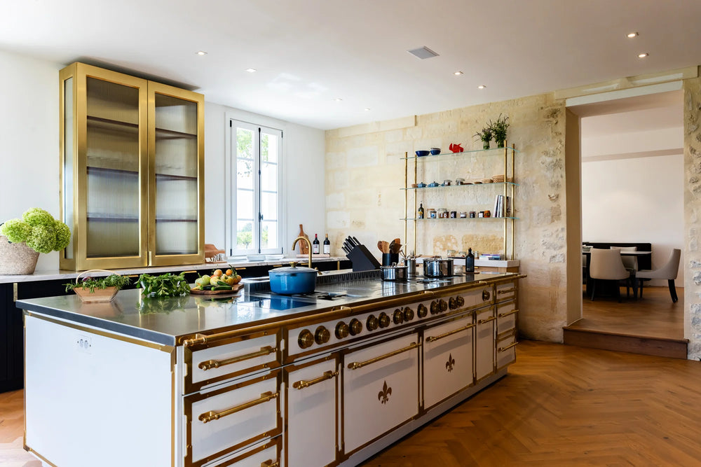 Luxury French Kitchen Range island in white with gold hardware and exposed stone walls.