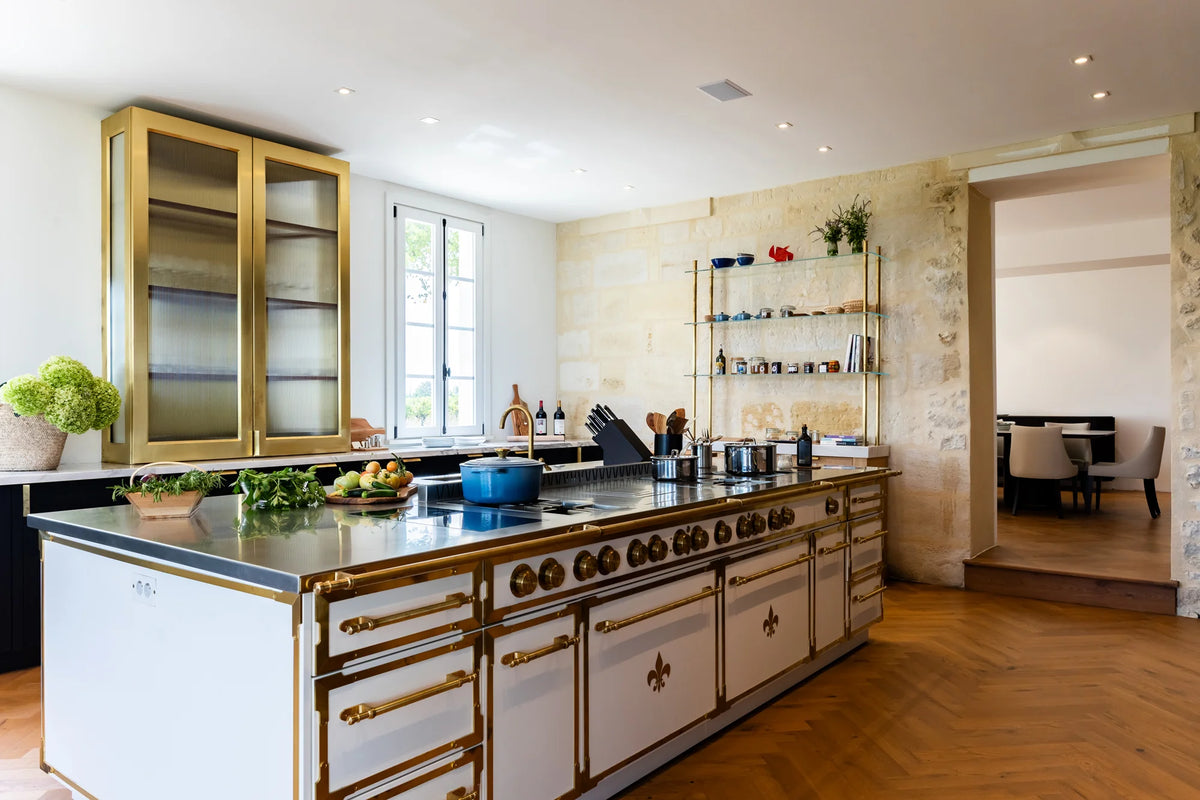 Luxury French Kitchen Range island in white with gold hardware and exposed stone walls.