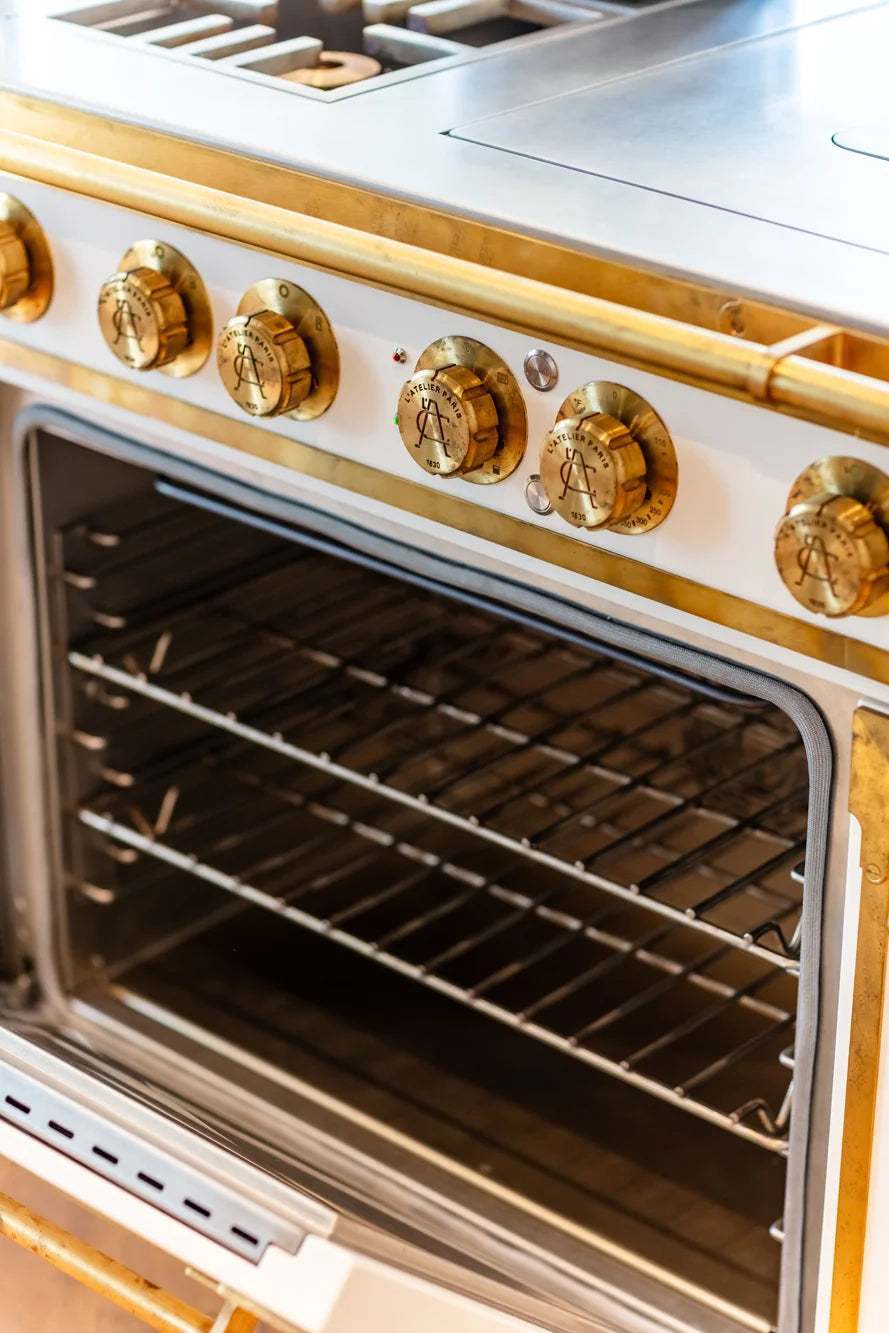 Professional Gas Range with an open oven interior and gold L'Atelier Paris control knobs.