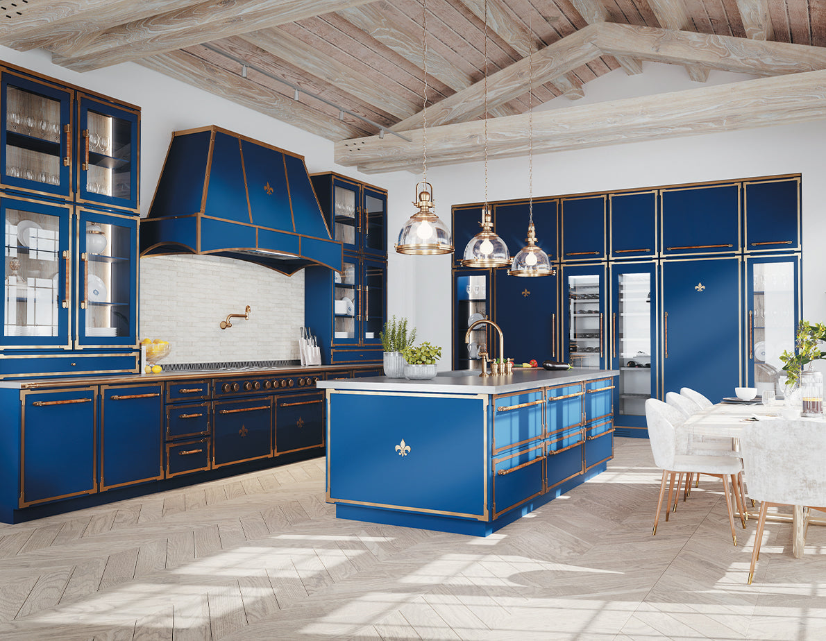 A magnificent, spacious kitchen designed in a bold blue and gold French-inspired style. It features a large blue island with gold trim and a fleur-de-lis accent, a matching blue professional range and hood, and abundant blue cabinetry with gold hardware, some with glass fronts. The room has a light wood floor, exposed beam ceiling, and a dining area with a long white table and chairs.