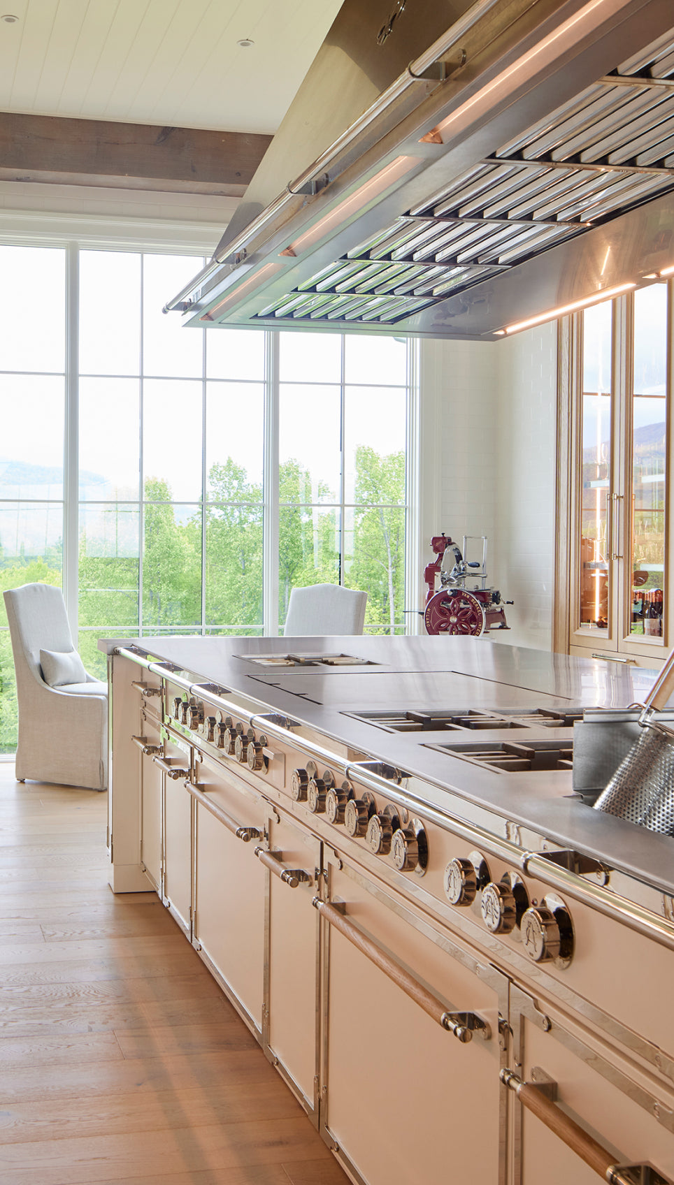 Luxury custom French kitchen range with polished metal finish and large cooking surface, set in a sunlit open-concept kitchen.