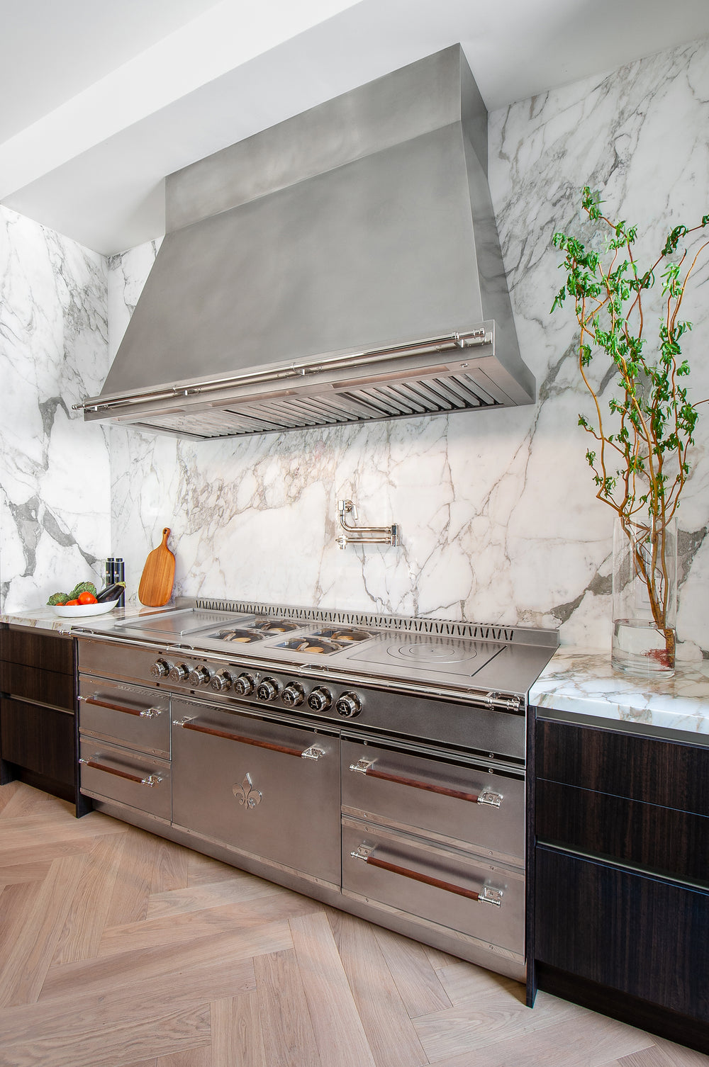 A professional-grade stainless steel kitchen range and large vent hood installed against a dramatic white and gray marble slab backsplash
