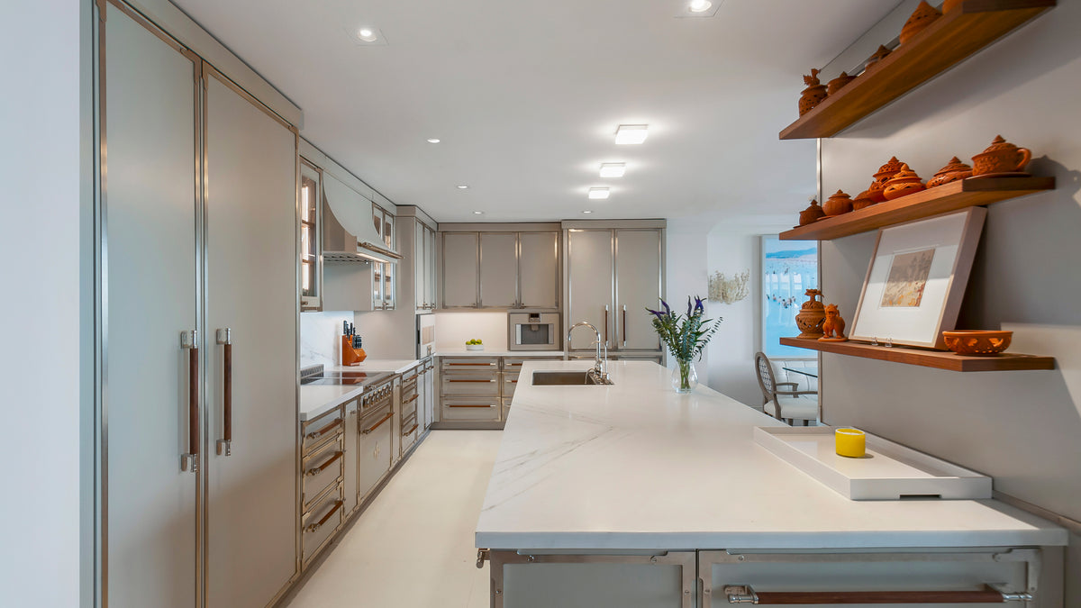 Luxury galley kitchen with polished light gray metallic cabinets, white marble-look quartz countertops, modern stainless steel and brass appliances, and an open dining area