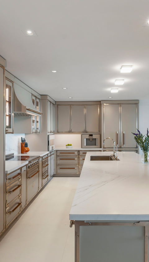Contemporary galley kitchen design featuring light taupe metallic cabinetry, chrome and wood hardware, professional range, and a large central island with undermount sink