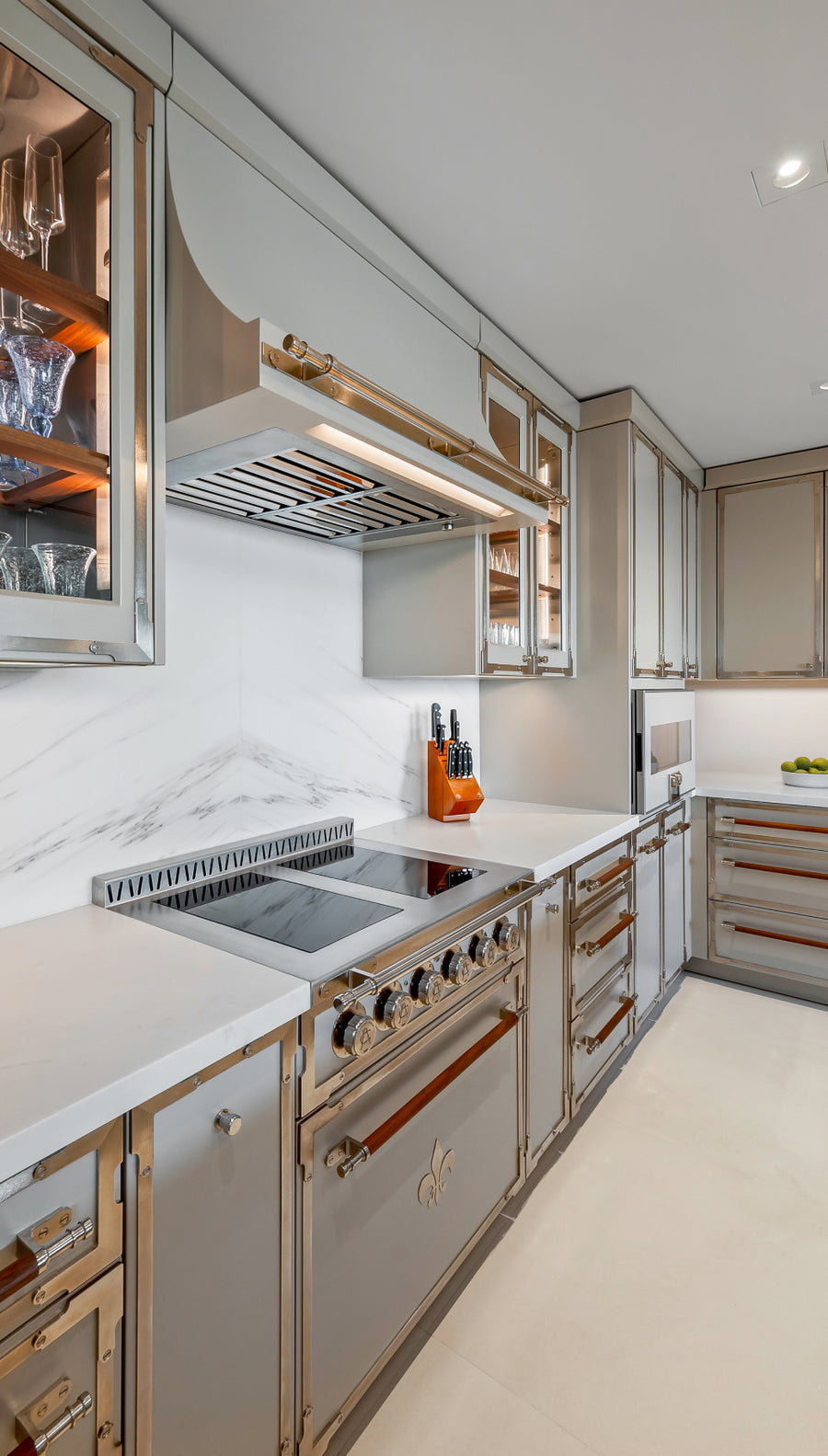 Professional-grade stainless steel kitchen range and custom metallic vent hood set against a white marble wall in a luxury kitchen.