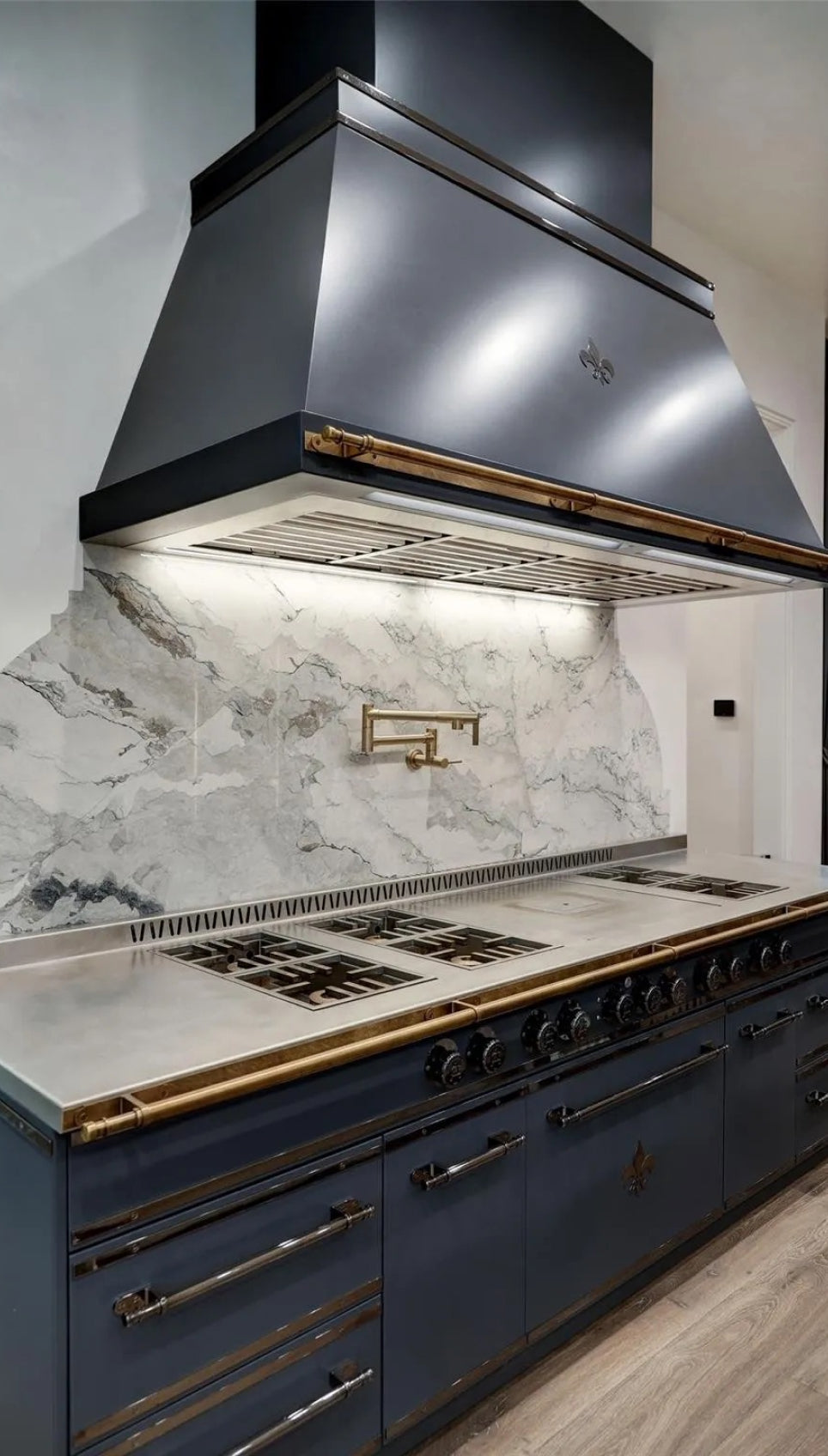 A sleek, dark blue professional kitchen range with brass accents, a large matching range hood, and a stunning white marble backsplash.