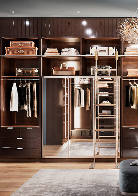 Dark wood walk-in closet with hanging racks, drawer storage, and sliding ladder in luxury dressing room.