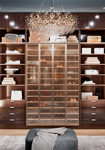 Luxury closet with glass shoe display cabinet, wood shelving, and crystal chandelier.