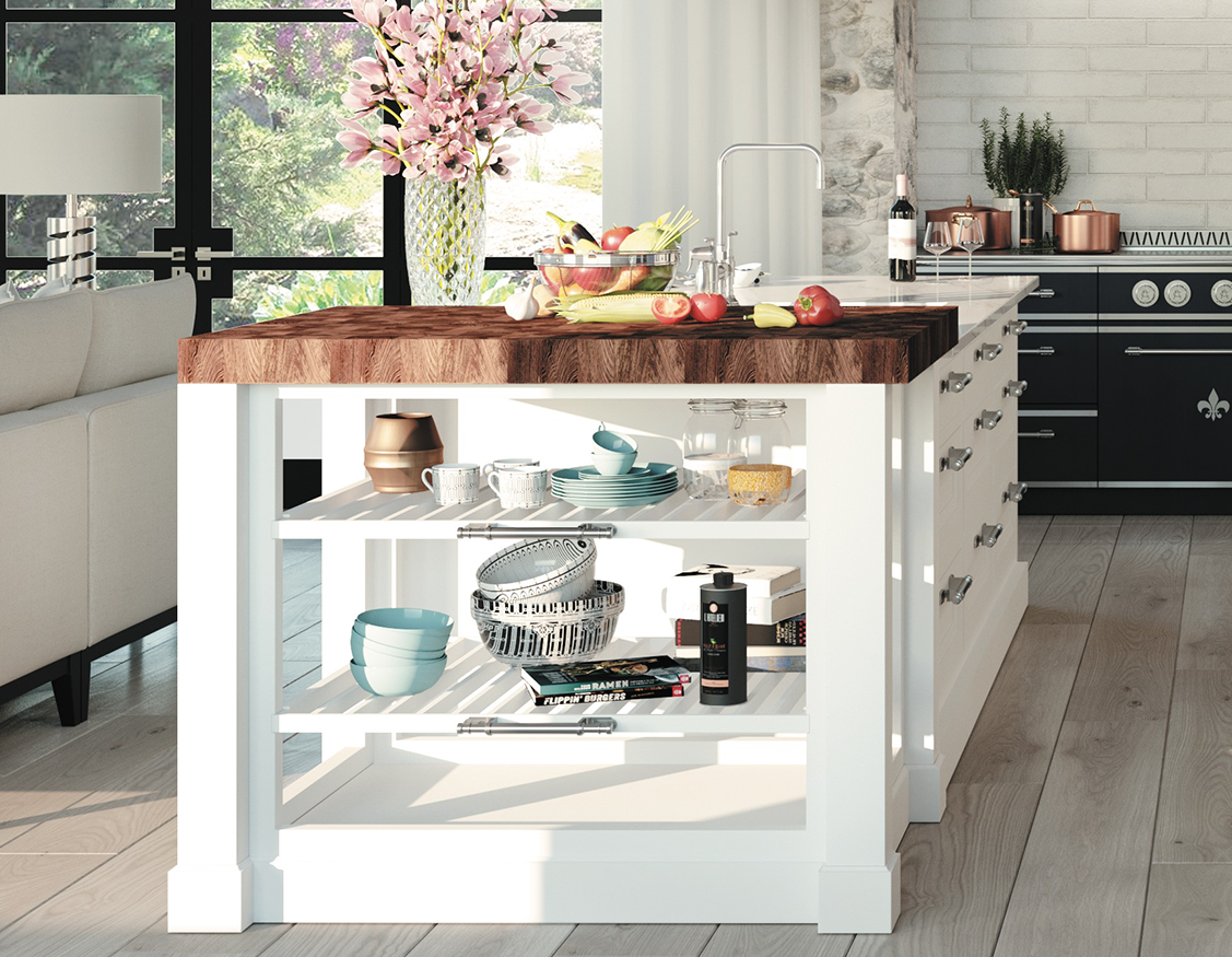 Close-up of a white kitchen island with a thick dark butcher block countertop and open shelving filled with cookbooks, bowls, and mugs. In the background is a large black-grid window with pink flowers, a white sofa, and the edge of a navy blue La Cornue range.