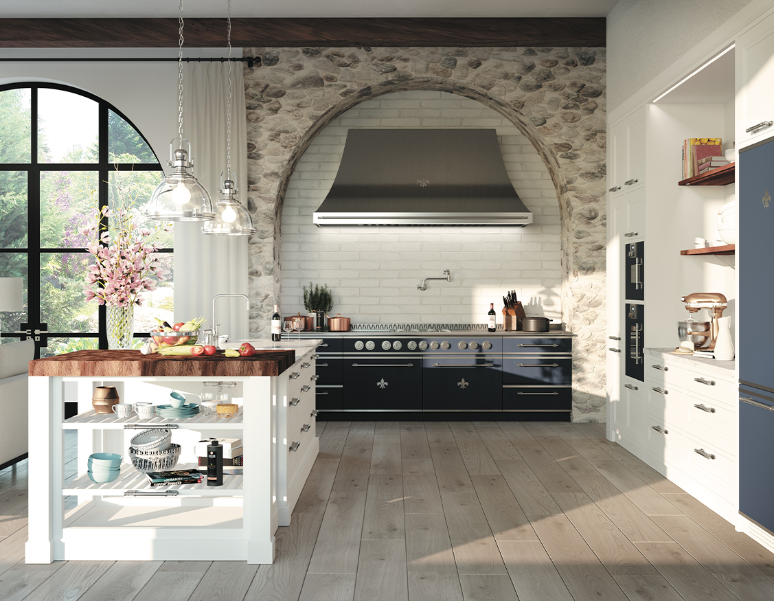 Elegant French country kitchen with a central white island topped with butcher block, facing a navy blue range and stainless steel hood set within a rustic stone arch