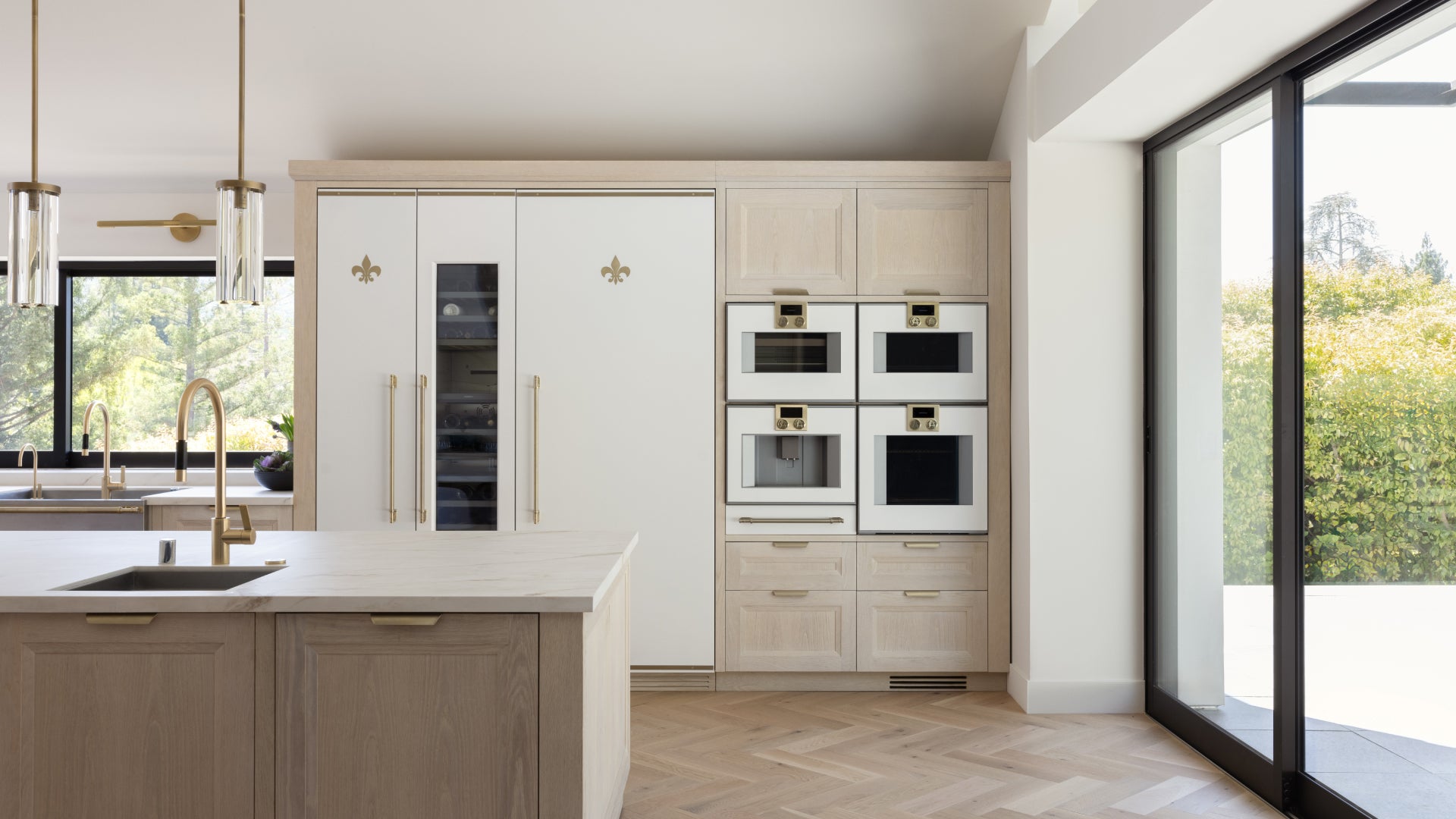 Modern French-style kitchen with built-in white and brass appliances, dual wall ovens, wine cooler, and light wood cabinetry.