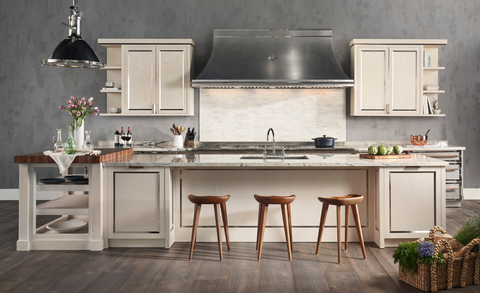 Off White Base Kitchen Cabinets With Marble Countertops and Wooden Stools. Silver Kitchen Hood in between Off White Wall Cabinets