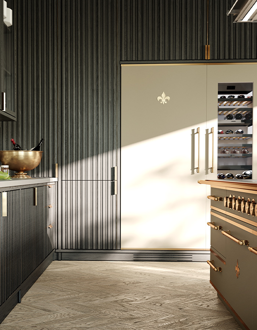 Vertical view of a luxury kitchen corner featuring a tall light-beige integrated refrigerator or wine column with a gold Fleur de Lis emblem and brass hardware, set against a striking dark-grey fluted wall paneling and base cabinetry, with a taupe and brass La Cornue range visible on the right.