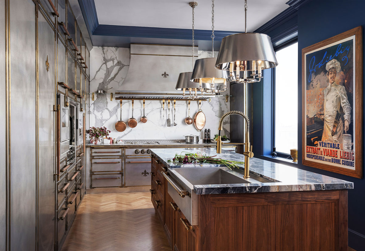 Marble kitchen island with sink and wooden base cabinet in the middle of the kitchen, with a silver French range and hood