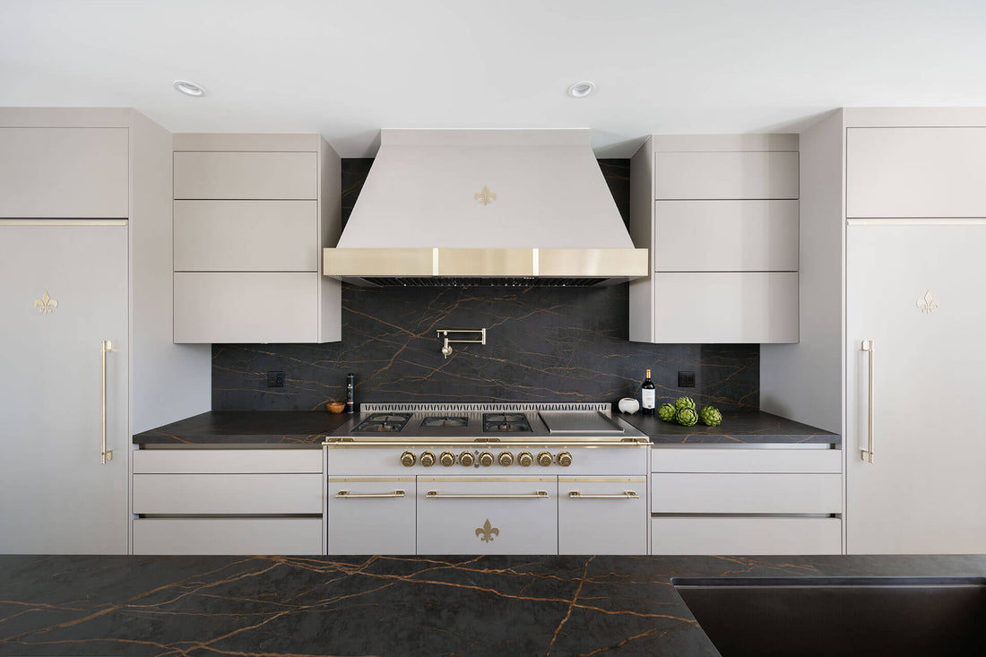 A white French luxury range with gold burners and handles beneath a custom hood between white cabinetry