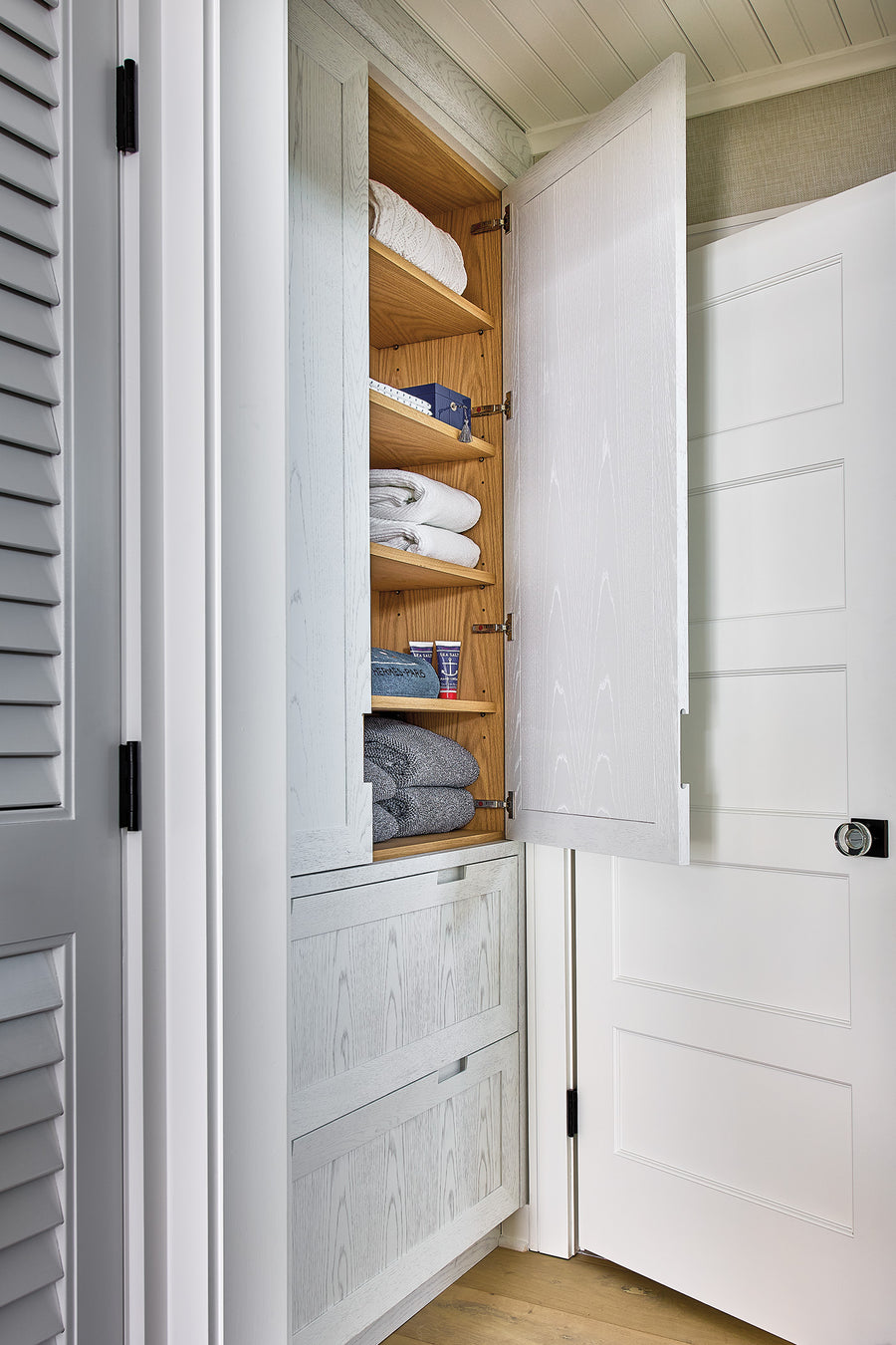 Handcrafted linen closet with wood shelving, folded towels, and louvered doors.
