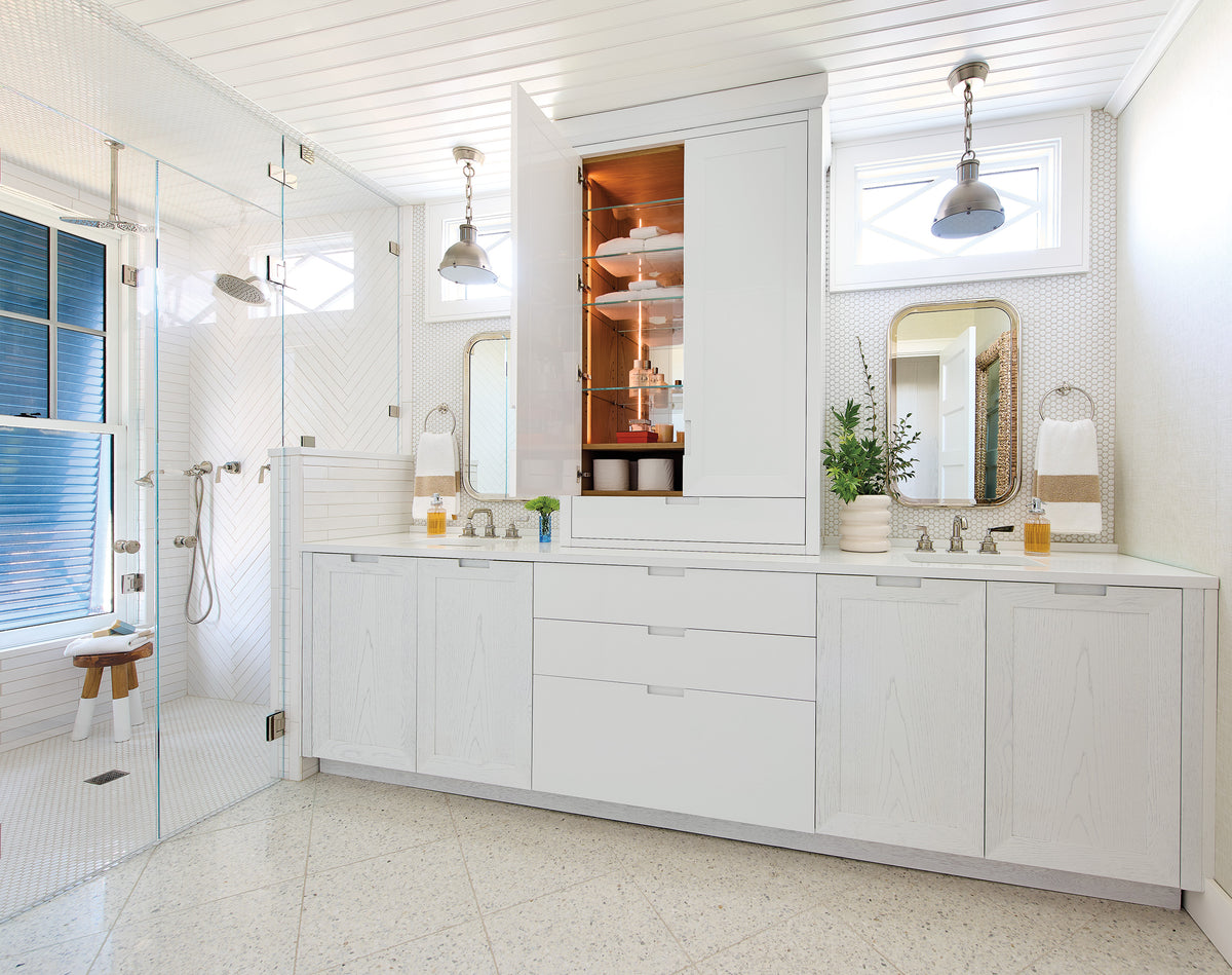 White double vanity bathroom with glass shower, penny tile, and built-in linen storage cabinet.