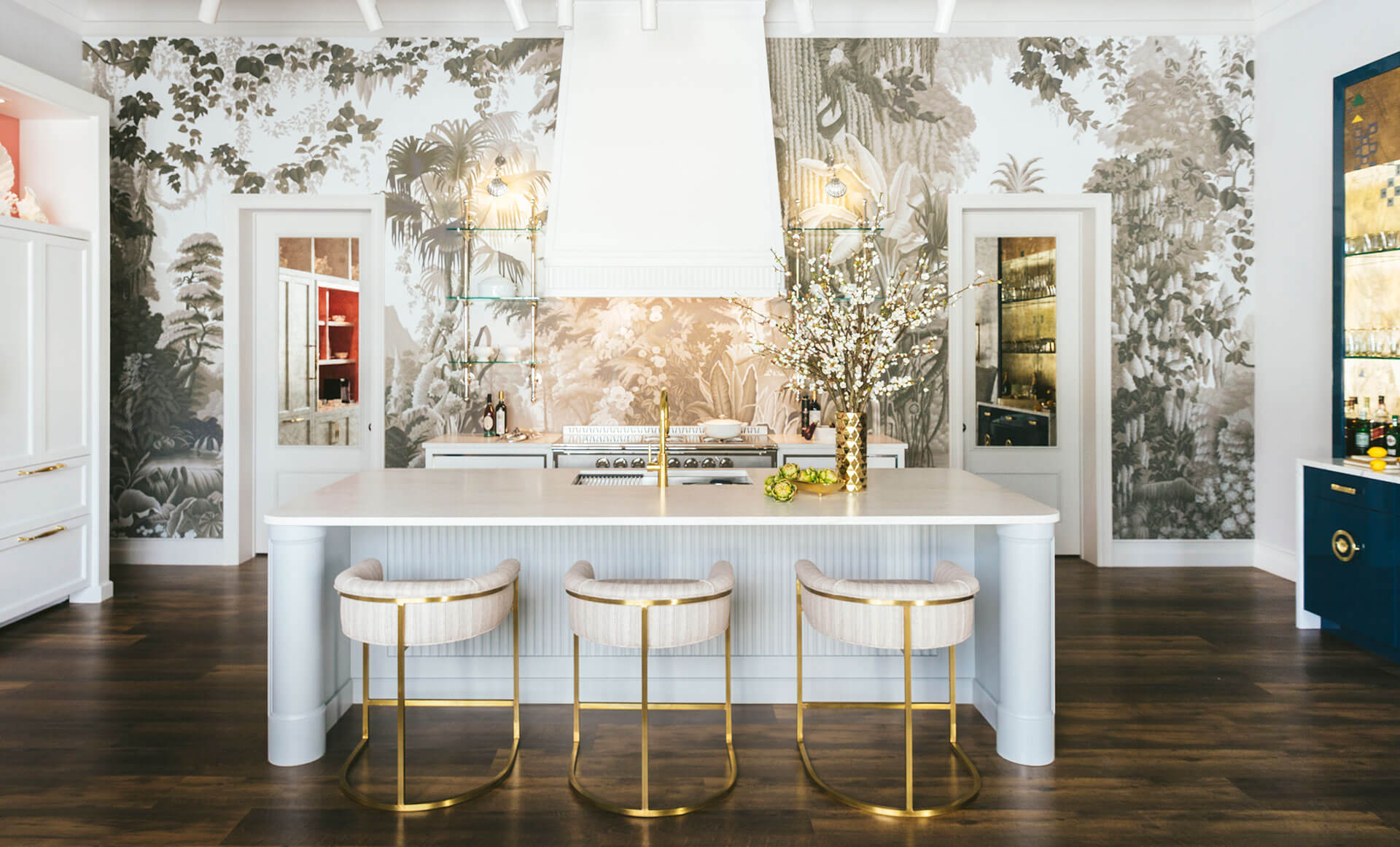 In the middle of Kitchen White Kitchen Countertop and Base Cabinets With White Chair Seat With Golden legs. White Kitchen Hood and Printed Kitchen Walls