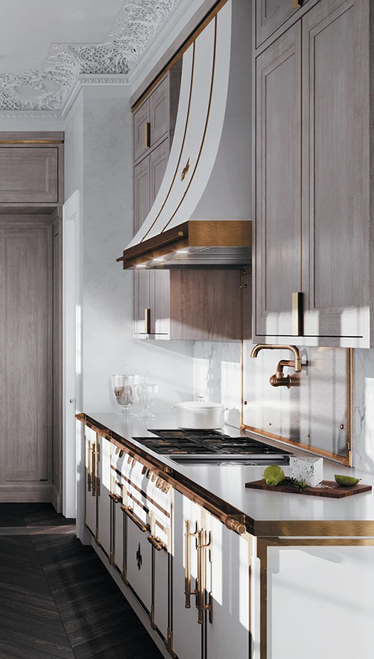 L'Atelier Paris white professional French range with copper trim and fleur-de-lis accents, featuring a matching custom range hood, weathered wood cabinetry, and a copper pot filler over a white marble countertop.