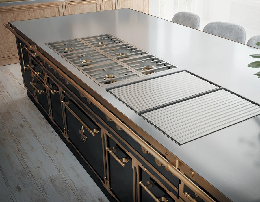 A luxurious close-up of a black kitchen island featuring a professional cooktop with a stainless steel surface, integrated gas burners, and a griddle. The island is highly detailed with polished brass trim and handles, including a prominent towel bar, and a fleur-de-lis emblem on the paneling.