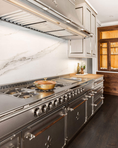 Silver classic kitchen ranges and copper cookware on French stove and custom kitchen hood above the stove range 